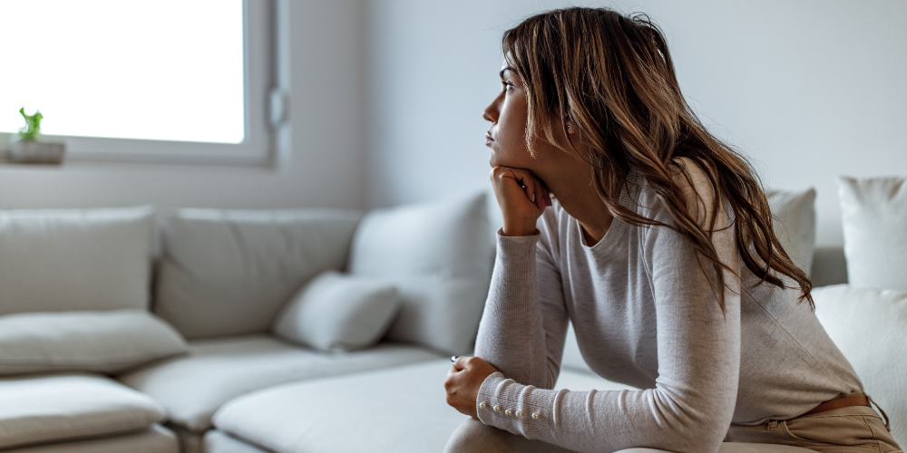 A woman resting her chin on her hand sits looking into the distance looking stressed