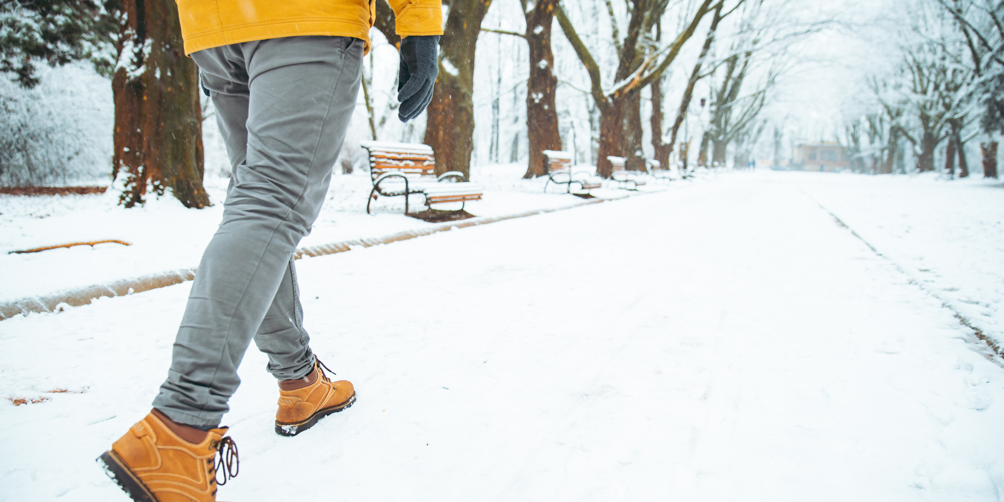 A person walking through snow in boots, jeans, and a bright yellow jacket.