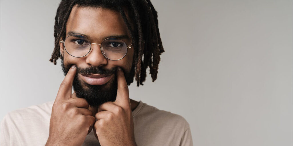 A man demonstrating toxic positivity by holding up his mouth to form a fake smile.