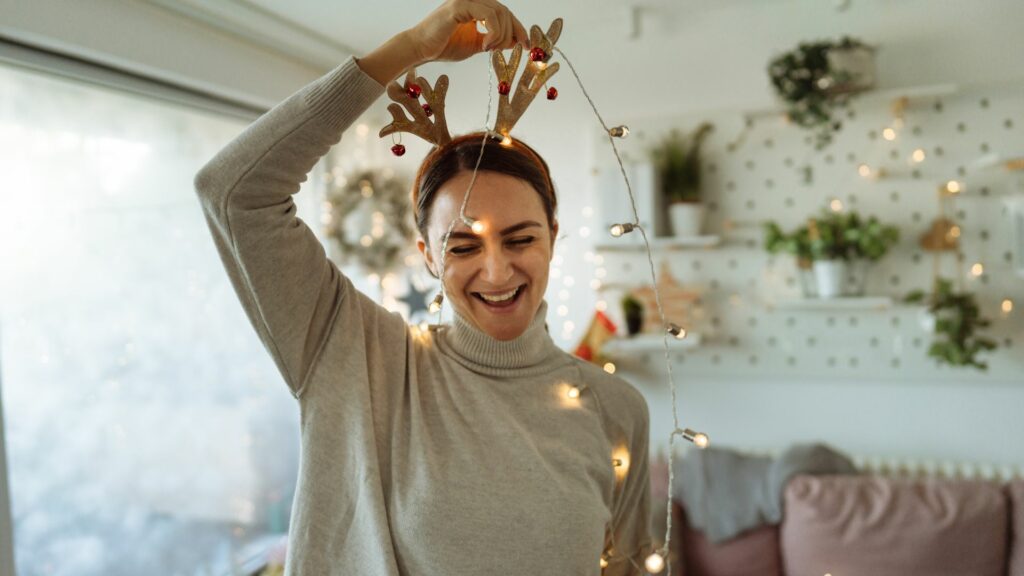 Woman joyfully hanging string lights while wearing an antler headband