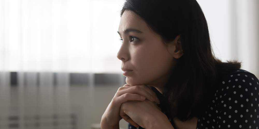 A woman gazing into the distance with her hands folded under her chin.