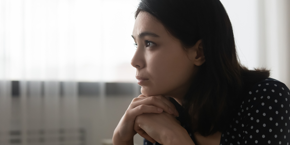 A woman gazing into the distance with her hands folded under her chin, demonstrating someone experiencing gaslighting.