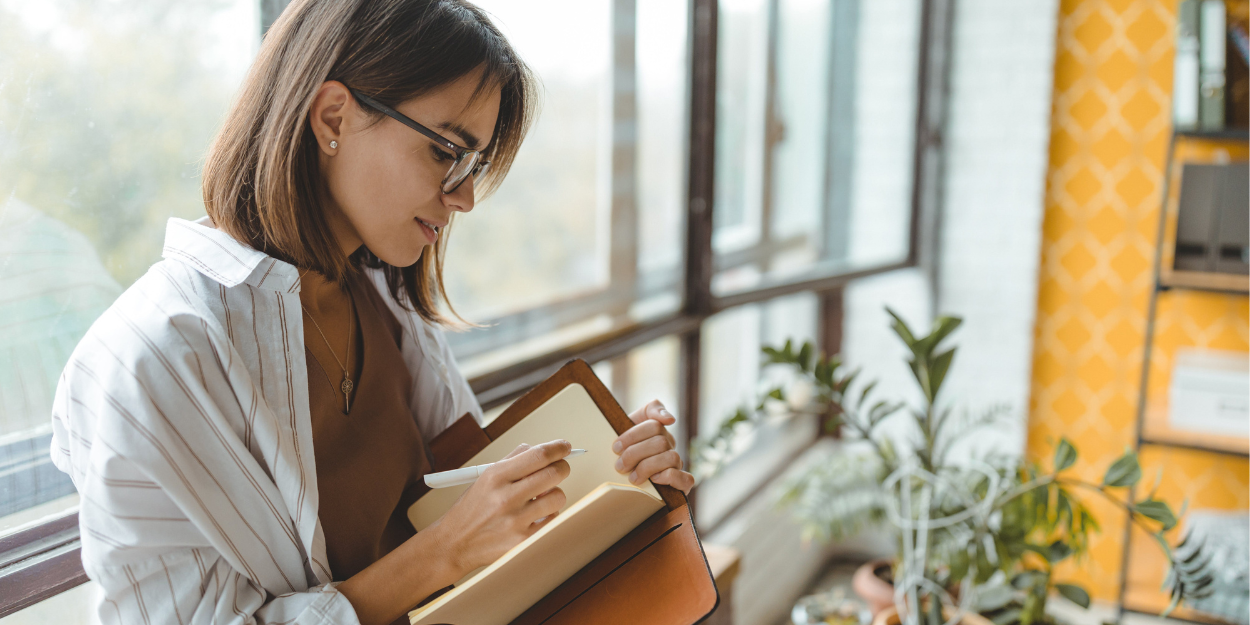 A woman sitting in front of a large window journaling, using the Four Options.