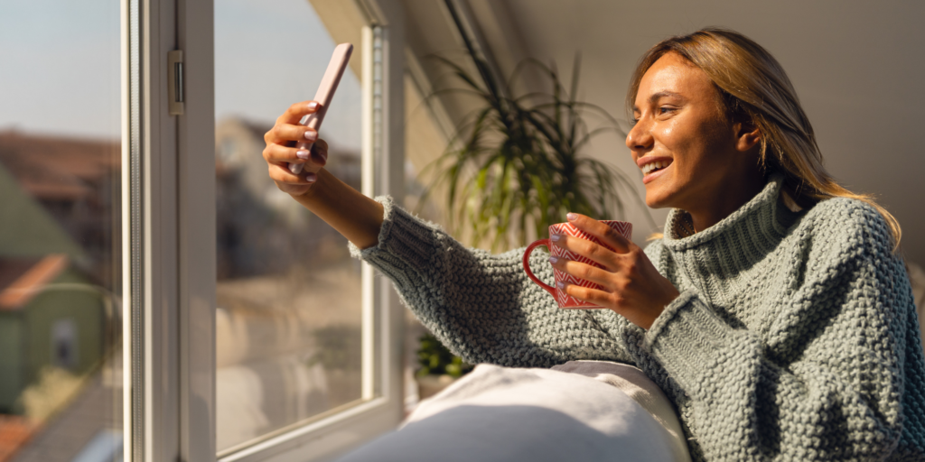 A woman in front of a bright window demonstrating instant gratification, by being on her phone.